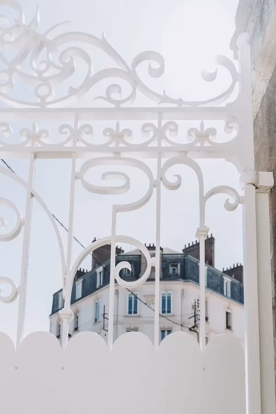 Détail des volutes en fer forgé restaurées et repeintes en blanc d'un portail rénové par Coyac à Nantes, avec tôle festonnée d'occultation en partie basse