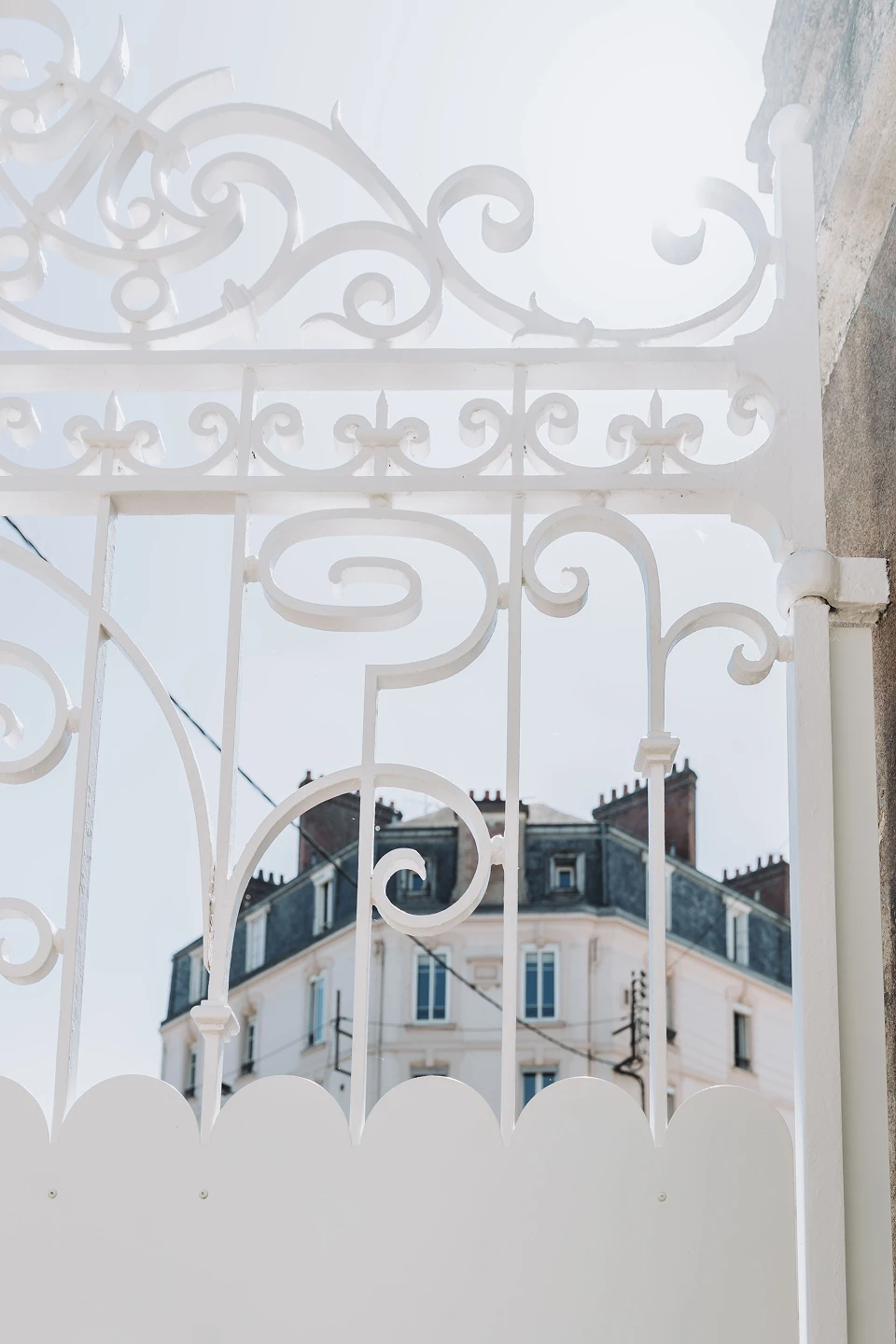 Détail des volutes en fer forgé restaurées et repeintes en blanc d'un portail rénové par Coyac à Nantes, avec tôle festonnée d'occultation en partie basse