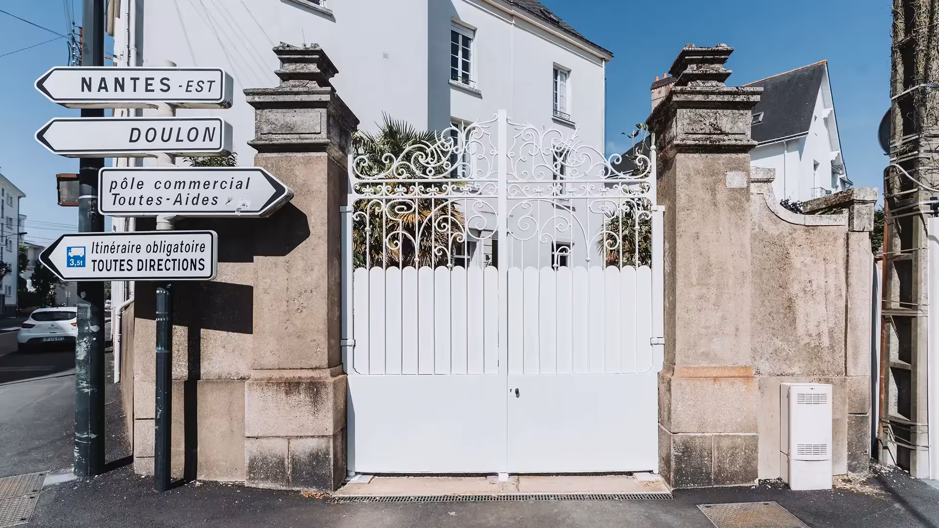 Portail ancien en fer forgé entièrement rénové et repeint en blanc par Coyac, entre piliers en pierre à Nantes, avec occultation par tôles festonnées