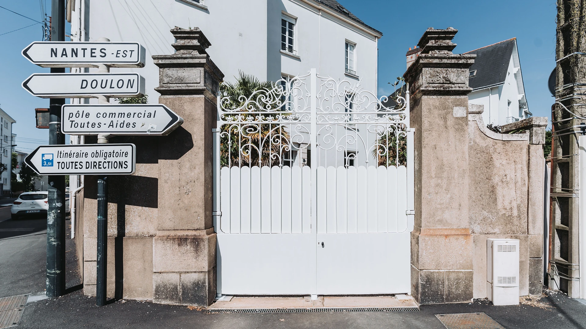 Portail ancien en fer forgé entièrement rénové et repeint en blanc par Coyac, entre piliers en pierre à Nantes, avec occultation par tôles festonnées