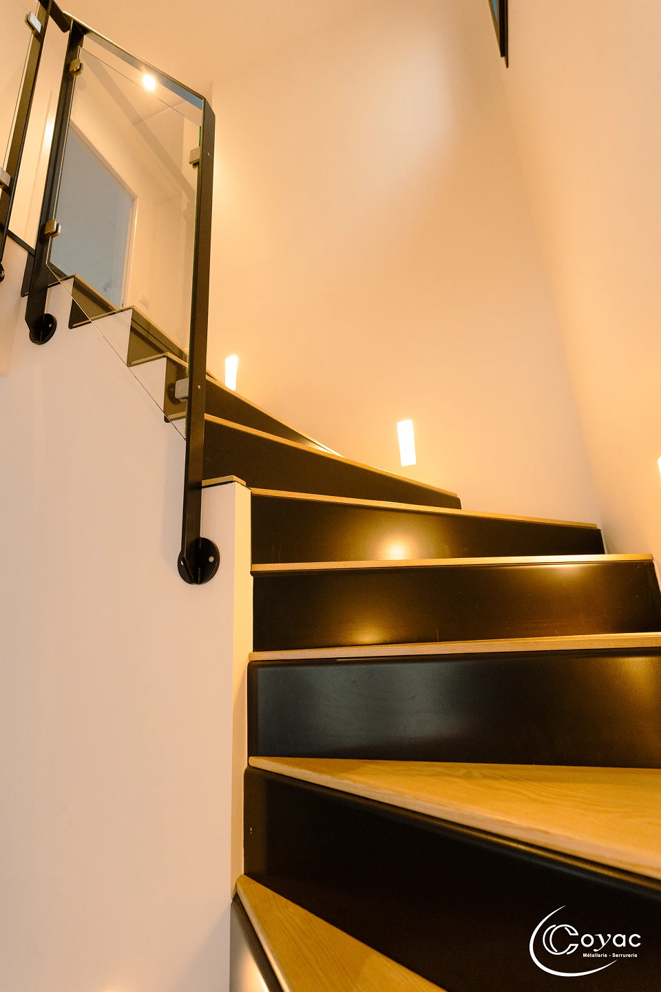 Vue ascendante d'un escalier sur-mesure métal et bois à Savenay, garde-corps vitré et main courante en acier noir, signé Coyac
