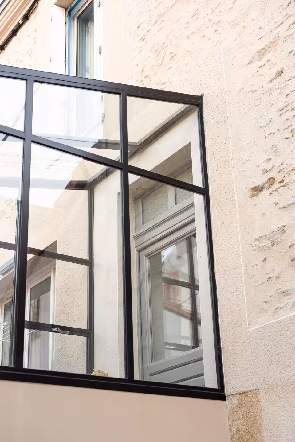 Angle d'une verrière sur-mesure en métallerie noire encastrée dans une façade en pierre à Trentemoult