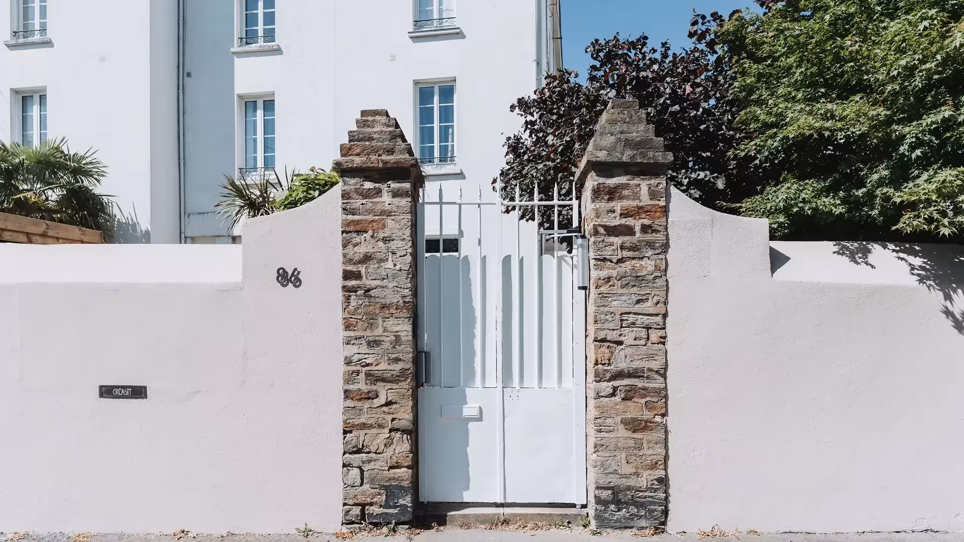 Portillon en fer forgé rénové et modernisé par Coyac à Nantes, repeint en blanc avec tôle festonnée et contrôle d'accès, intégré entre piliers en pierre