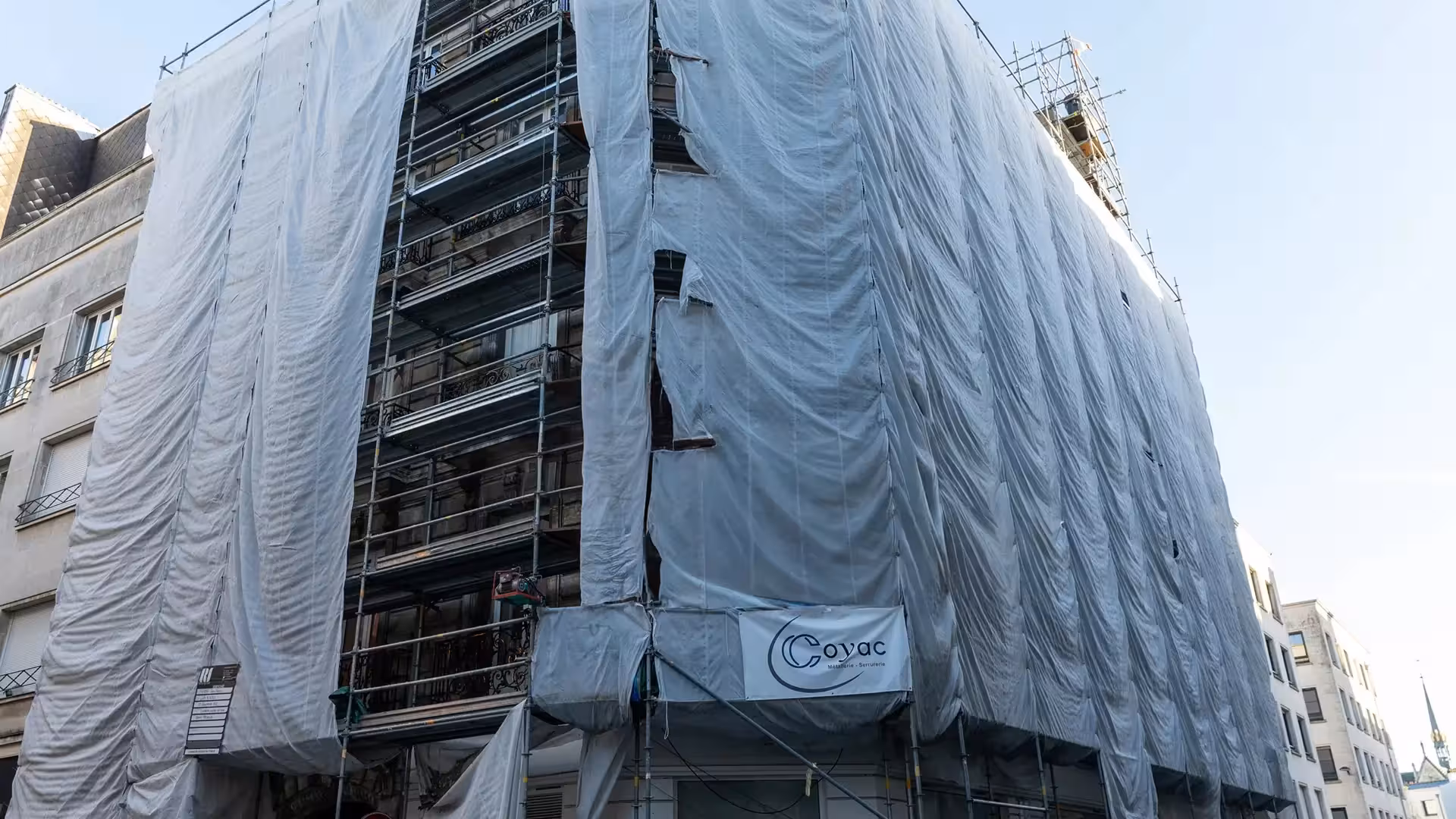 Façade entière d'un immeuble de caractère sous échafaudage et bâche de chantier dans le quartier Graslin à Nantes, projet de restauration mené par Coyac
