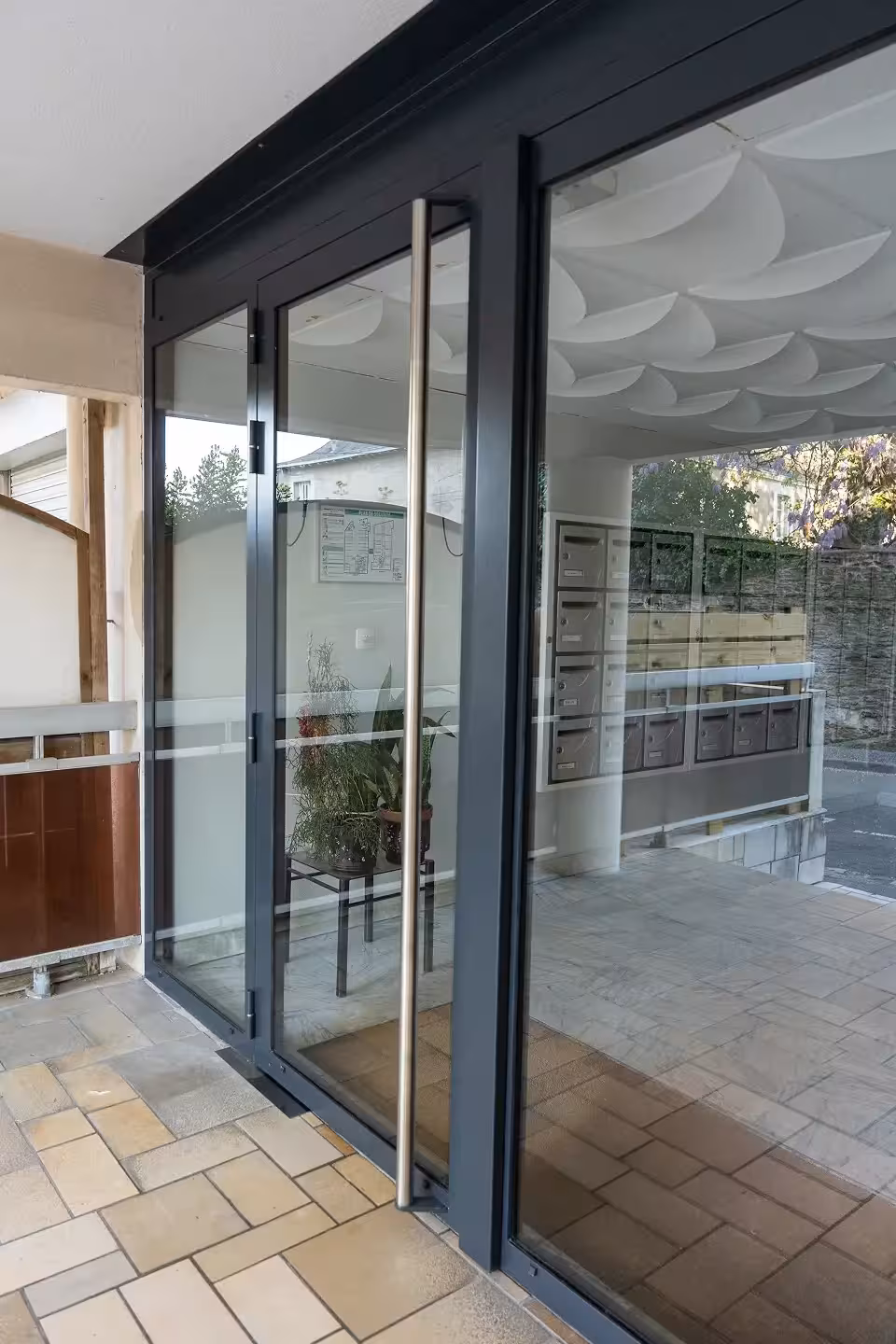 Vue trois-quarts depuis l'intérieur du hall d'un immeuble nantais montrant la porte menuisée en acier avec poignée inox, posée par Coyac