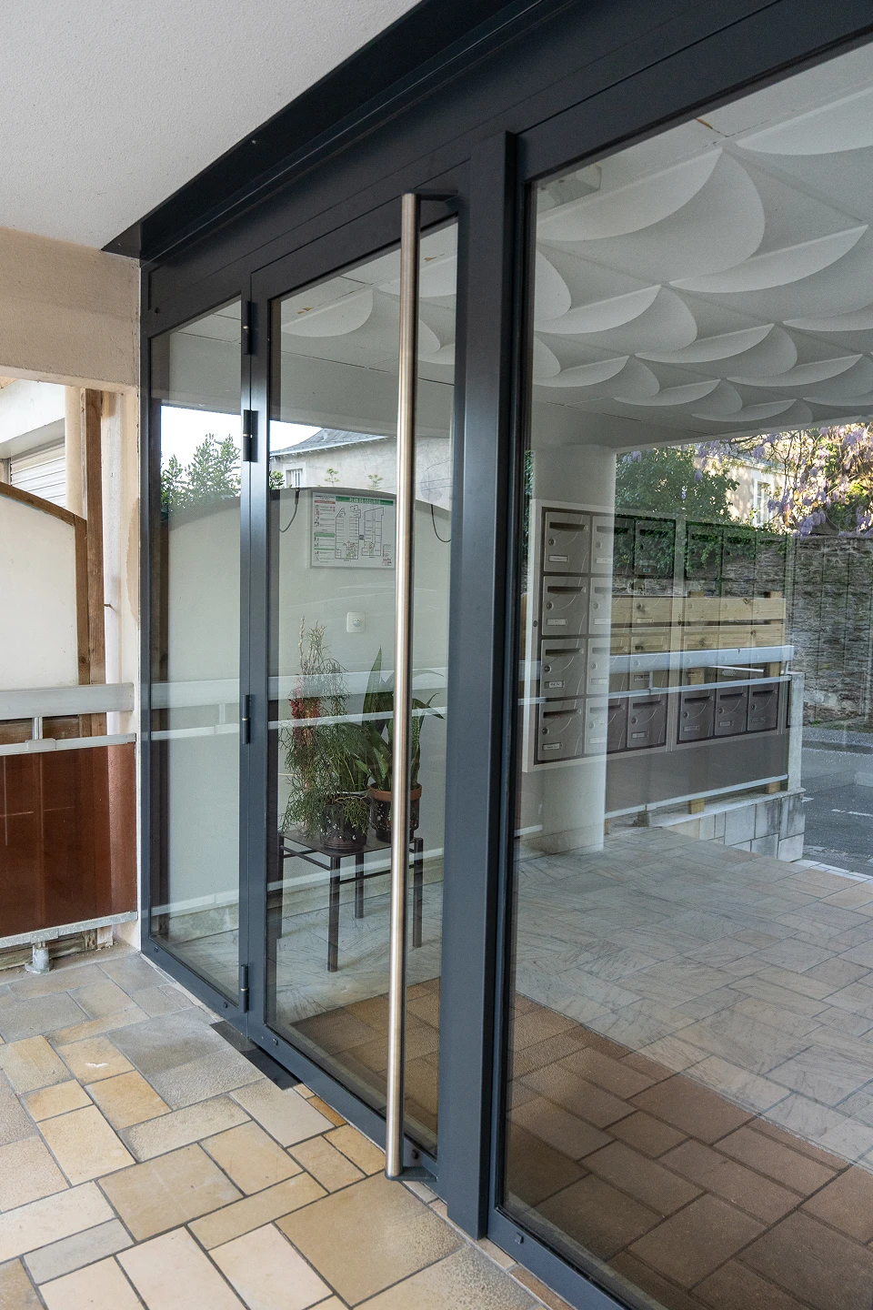 Vue trois-quarts depuis l'intérieur du hall d'un immeuble nantais montrant la porte menuisée en acier avec poignée inox, posée par Coyac