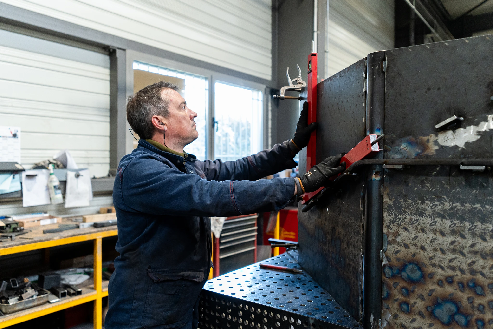 Compagnon métallier de Coyac contrôlant l'équerrage d'une structure en acier soudée sur table de soudure dans l'atelier de fabrication