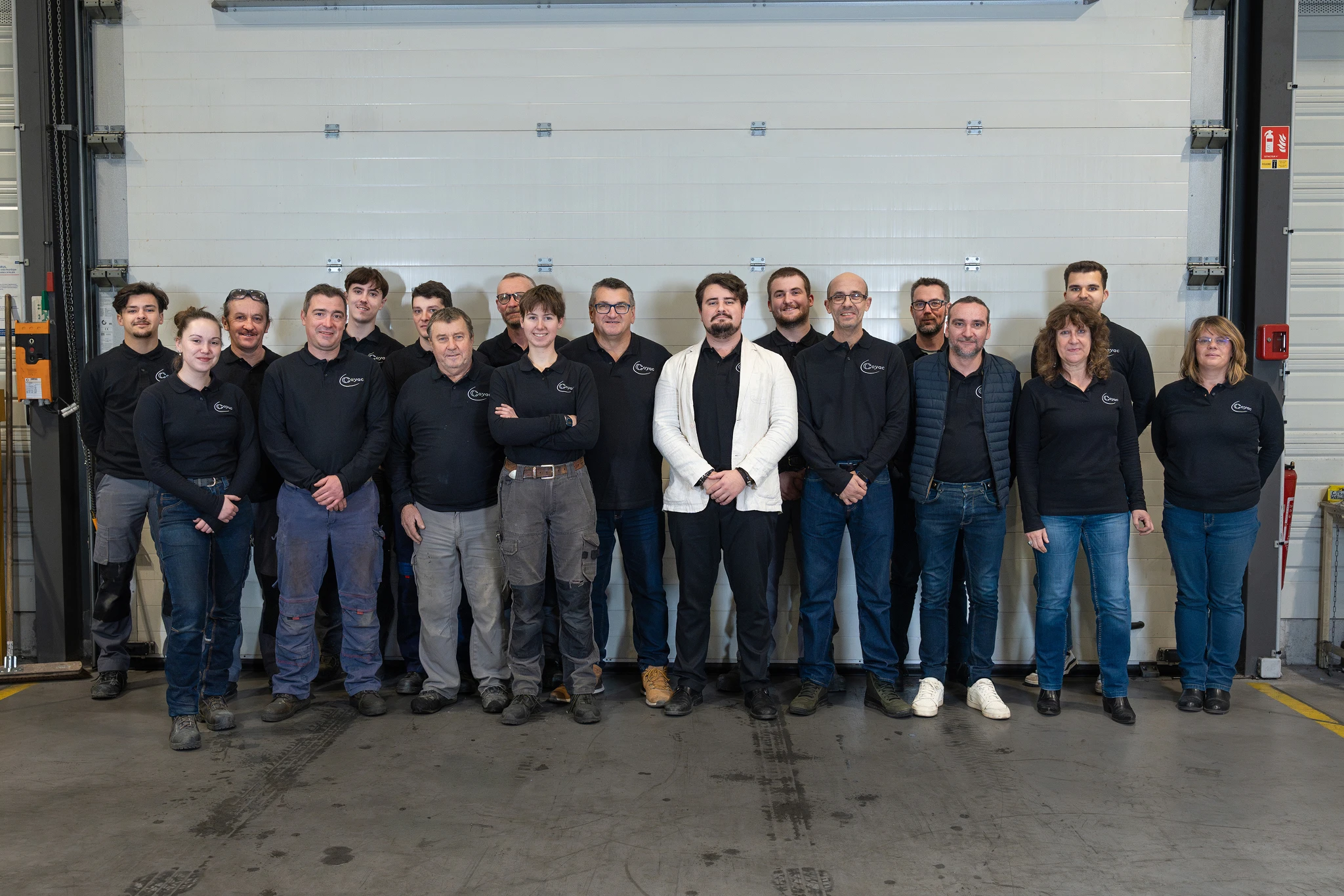 Photo de groupe de l'équipe Coyac réunie devant la porte de l'atelier, métalliers, ferronniers et équipe administrative