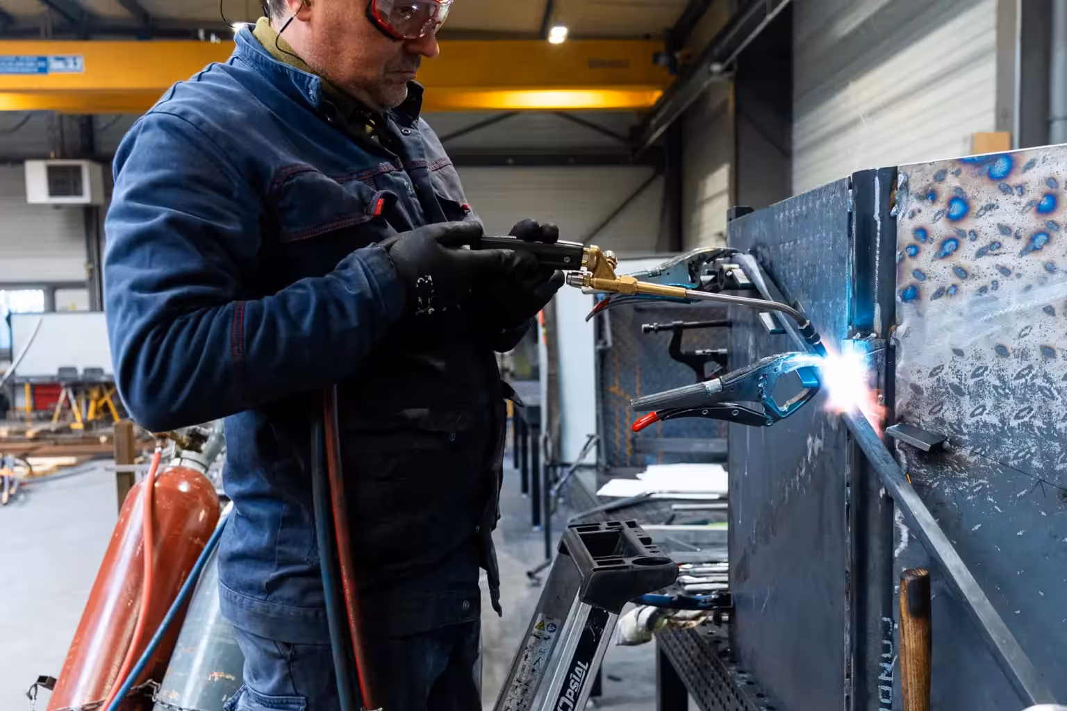 Compagnon métallier de Coyac soudant au chalumeau sur un ouvrage en cours d'assemblage dans l'atelier, étincelles et arc lumineux