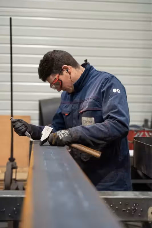 Compagnon métallier de Coyac travaillant au burin et au marteau sur une pièce métallique dans l'atelier de fabrication
